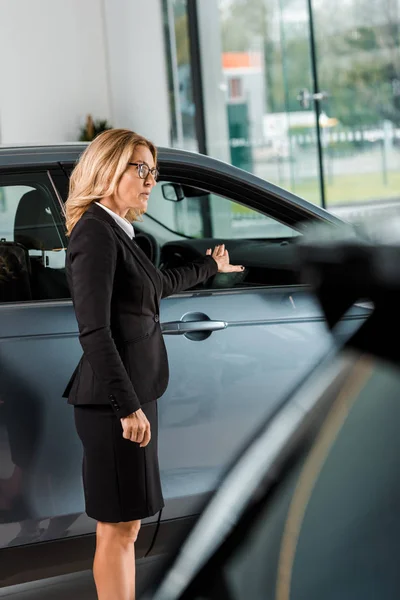 有吸引力的女汽车经销商指向汽车陈列室 — 免费的图库照片