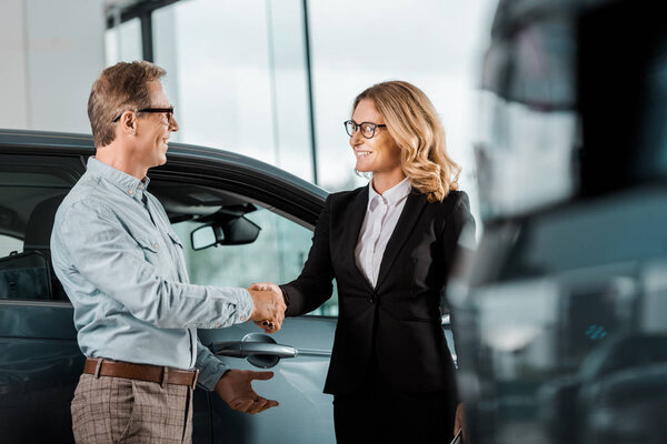 Adult customer and female car dealer shaking hands at showroom