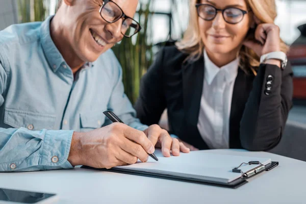 Lächelnde Erwachsene Kundin Unterzeichnet Vertrag Mit Autohändlerin Showroom — Stockfoto