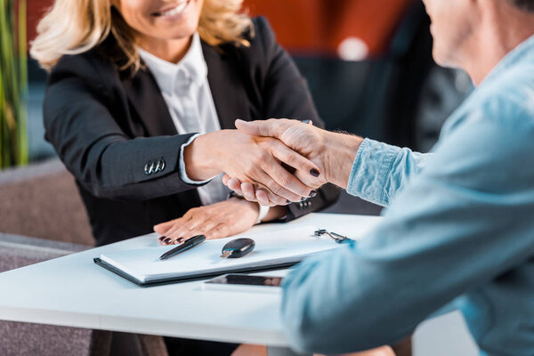 cropped shot of adult customer and female car dealer shaking hands in showroom