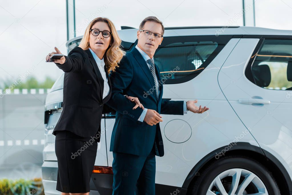 businessman and businesswoman pointing away while choosing new automobile in showroom