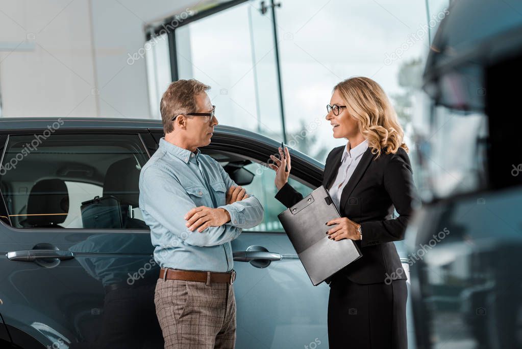 handsome adult man and female car dealer chatting at showroom