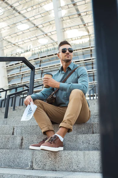 ローアングル サングラス行きコーヒーを保持していると階段の上に座っている間ビジネス新聞の人間観 — ストック写真