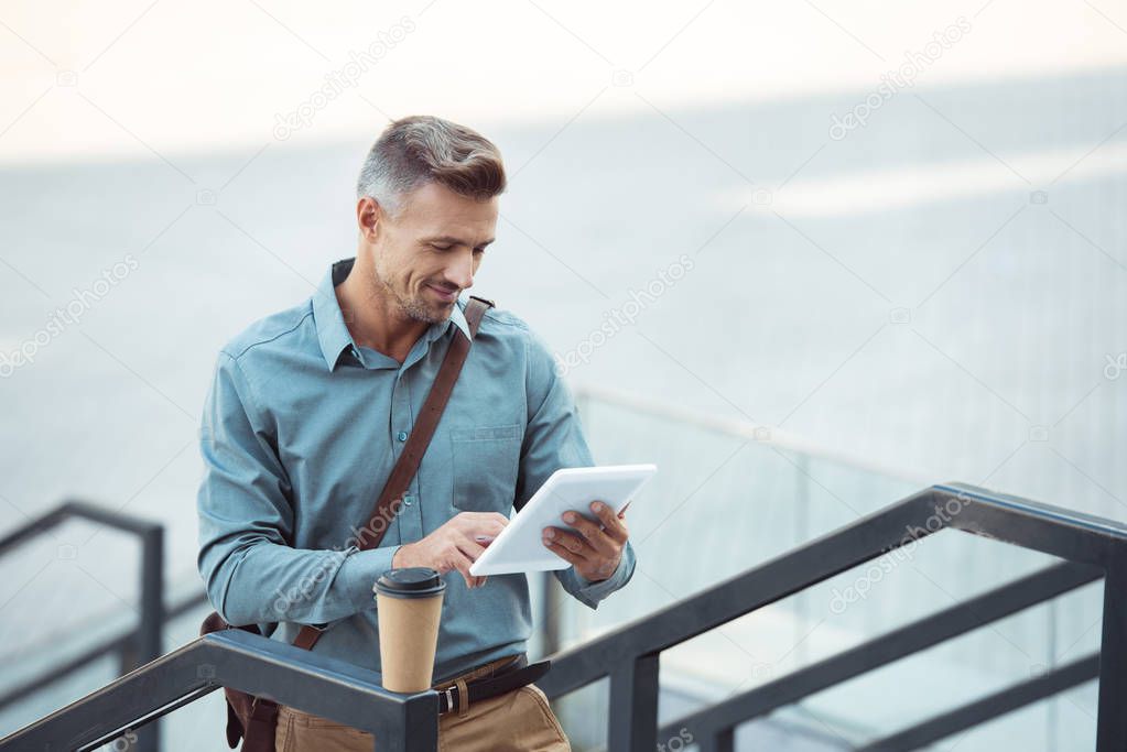 handsome smiling middle aged man using digital tablet on stairs