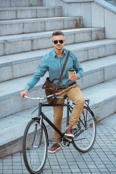 サングラスに行くコーヒーを保持していると路上自転車に座ってカメラ目線でハンサムな男  — 無料ストックフォト