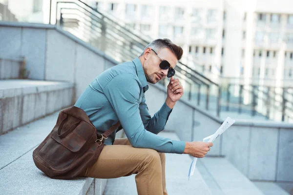 şık orta yaşlı işadamı ile gazete merdivenlerde oturan ve güneş gözlüğü ayarlama