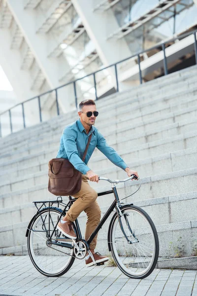 英俊的中年商人在太阳镜骑自行车在街上 — 图库照片