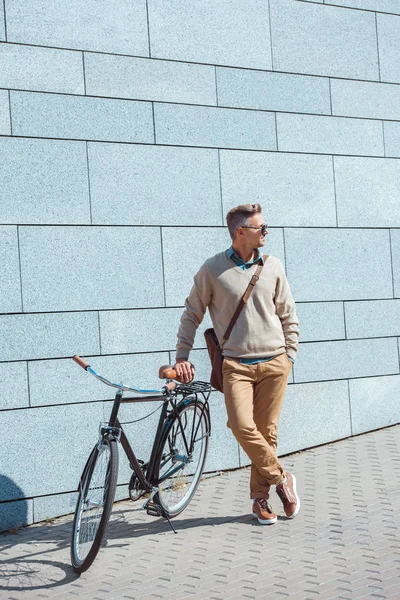 时尚的中年男子在太阳镜下靠在自行车上 看着走在街上 — 免费的图库照片