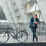 Framgångsrik mellersta åldern affärsman i formella slitage lutar på räcke nära cykel