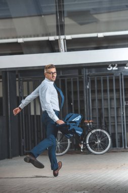 handsome middle aged buisnessman in eyeglasses looking at camera while hurrying up to bike  clipart