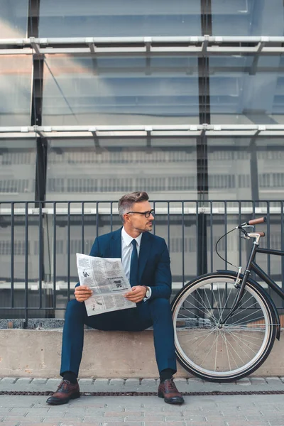 中央高齢者実業家新聞を押しながら路上自転車のそばに座って中よそ見 — ストック写真