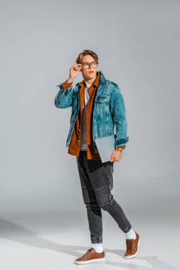 handsome stylish student posing in denim jacket with laptop on grey