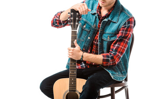 partial view of hipster man in denim vest sitting with acoustic guitar isolated on white