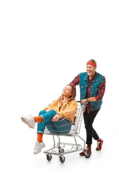 happy young man carrying shopping trolley with girlfriend isolated on white