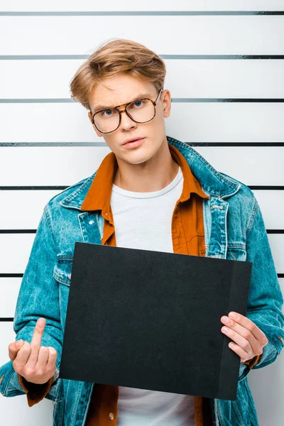handsome young man holding prison board while standing in front of police line up