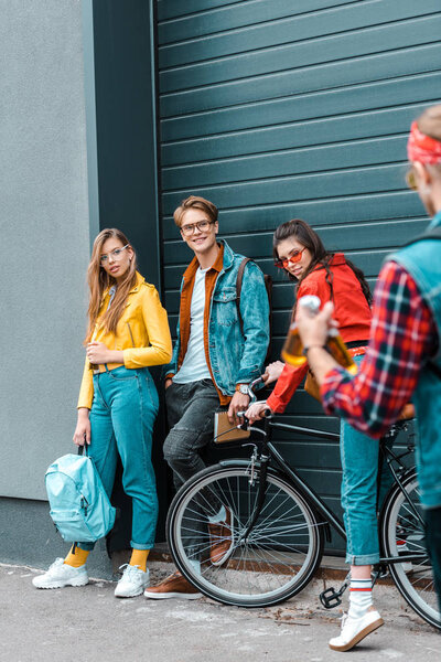 stylish male hipster brought beer for young smiling friends on street with bike