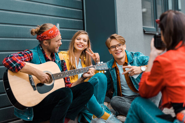 girl taking photo of hipsters with acoustic guitar on street