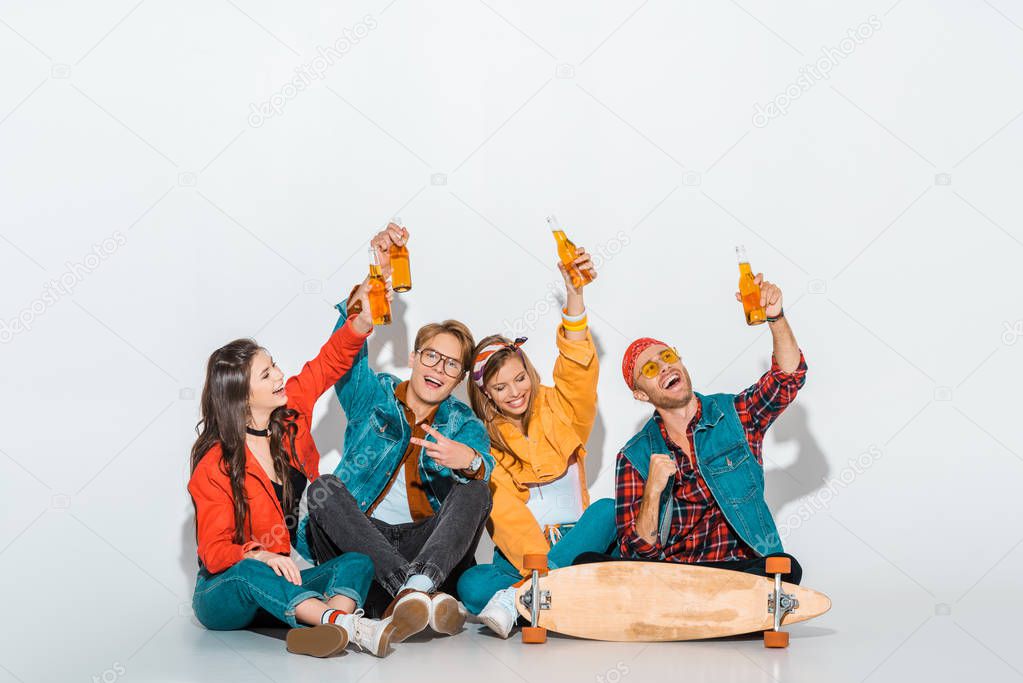 cheerful stylish hipsters sitting with skateboard and holding beer bottles