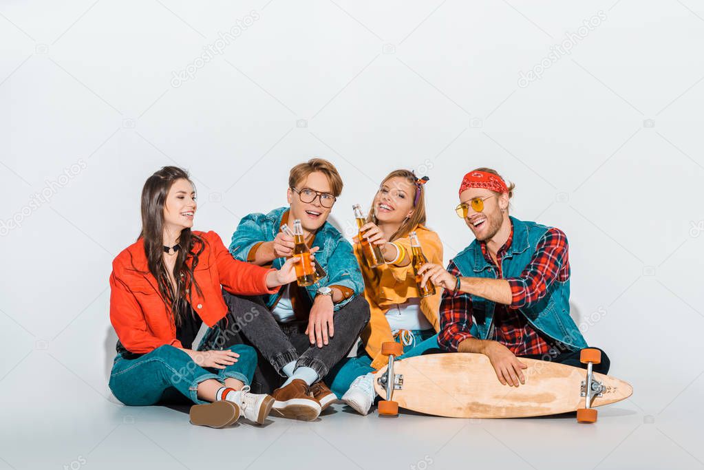 young stylish hipsters clinking with beer bottles and sitting with longboard 