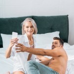 Lekfulla unga paret tar selfie tillsammans i sovrum