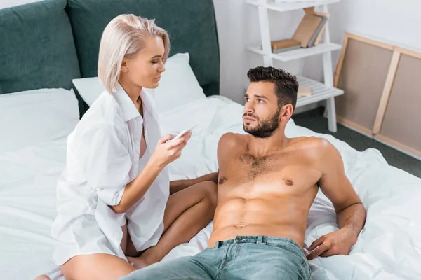 Attraktive Junge Frau Sitzt Mit Smartphone Über Ihrem Freund Bett — Stockfoto