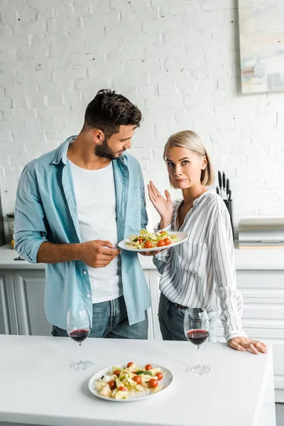 Irritado Namorada Sorrir Gestos Perto Namorado Com Prato Salada Cozinha — Fotos gratuitas