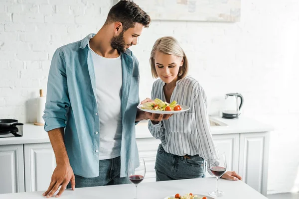 Namorado Mostrando Salada Prato Para Namorada Atraente Cozinha — Fotografia de Stock