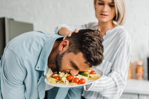 irritated girlfriend smashing boyfriend face into salad in kitchen