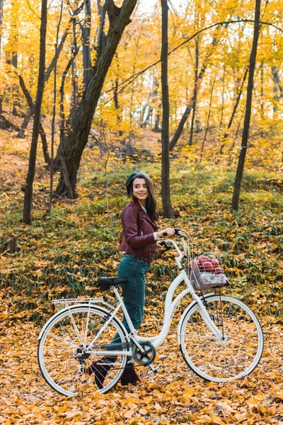 スタイリッシュな革のジャケット ベレー帽の森で自転車を運ぶ幸せのファッショナブルな女性 — ストック写真