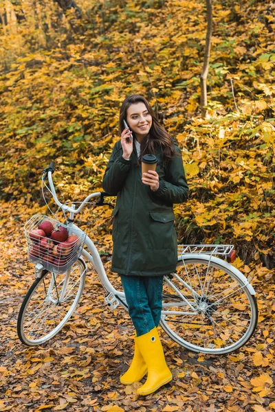 Smiling Young Woman Paper Coffee Cup Talking Smartphone Bicycle Autumnal — Stock Photo, Image