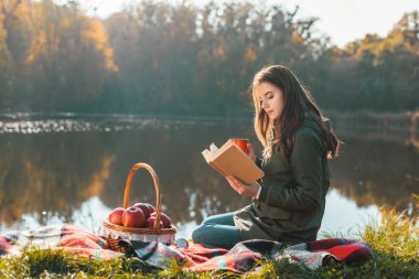 güzel genç kadın kahve fincanı battaniye gölet Park yakınındaki kitap okuma ile