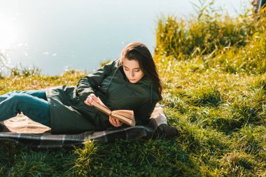 güzel kadın battaniye yakınındaki park su birikintisi üzerinde döşeme iken kitap okuma