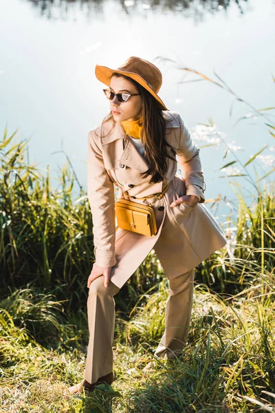 Elegante Donna Elegante Trench Cappello Occhiali Sole Posa Vicino Stagno — Foto stock gratuita