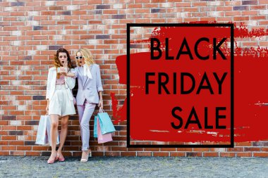 shocked young women with shopping bags taking selfie while standing in front of brick wall, black friday sale banner clipart