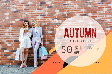 shocked young women with shopping bags taking selfie while standing in front of brick wall, autumn sale banner clipart