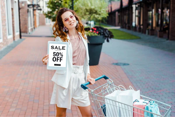 Beautiful Young Woman Shopping Cart Full Paper Bags Showing Tablet — Free Stock Photo