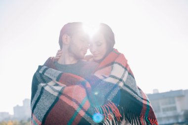 beautiful young couple covering in plaid and cuddling with sun shining behind clipart
