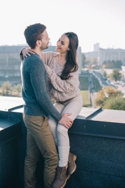 smiling young couple embracing and looking at each other on rooftop clipart