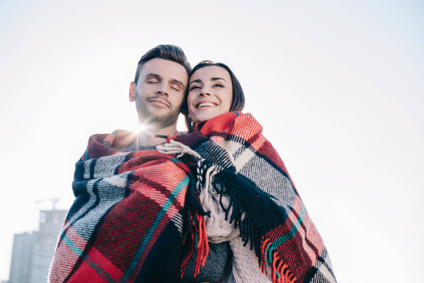 вид снизу на красивую молодую пару, покрытую клеткой и обнимающую солнце, сияющее сзади
