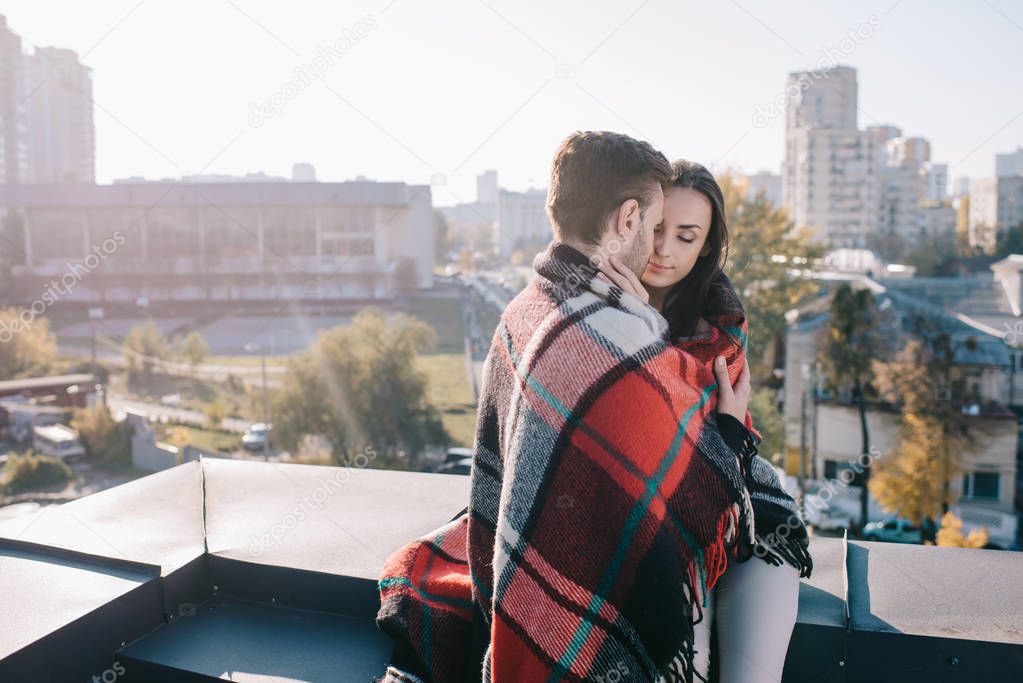 beautiful young couple covering in plaid and cuddling on rooftop