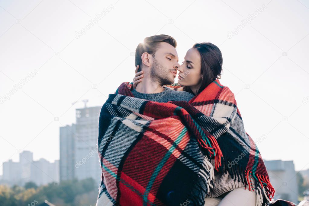 beautiful young couple covering in plaid and kissing with sun shining behind