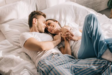 beautiful young couple in pajamas cuddling in bed in morning clipart