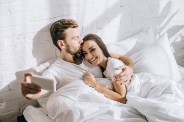 mutlu genç çiftin selfie smartphone ile sabah yatakta dinlenirken alarak yüksek açılı görünüş