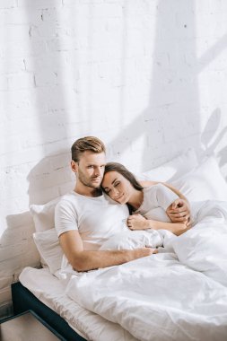 yatakta kız arkadaşıyla rahatlatıcı ve kameraya bakarak yakışıklı delikanlı