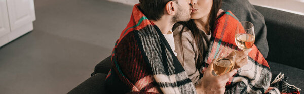 панорамный снимок молодой пары с бокалами белого вина расслабляющий и целующийся на диване под клеткой
