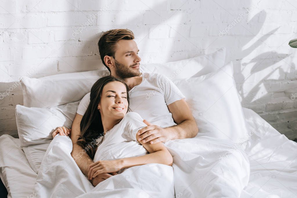 hansdome young man relaxing in bed with his sleeping girlfriend in morning