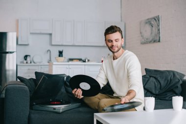 çekici bir genç adam kanepede otururken diskler için vinil plak çalar holding