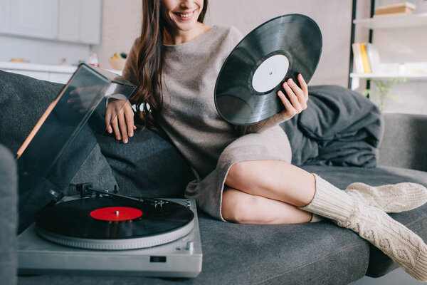 cropped shot of young woman listening music with vinyl record player on couch at home