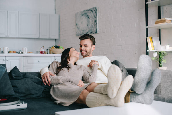 happy couple in woolen socks relaxing on couch at home