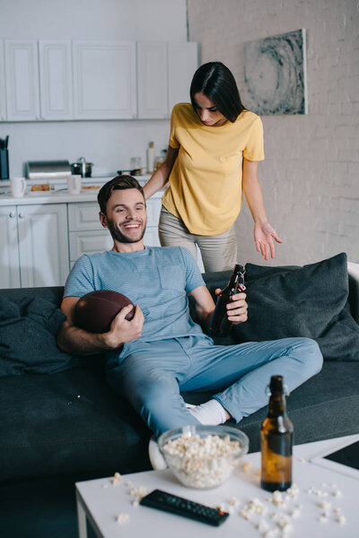angry woman yelling at husband while he watching american football on tv at home